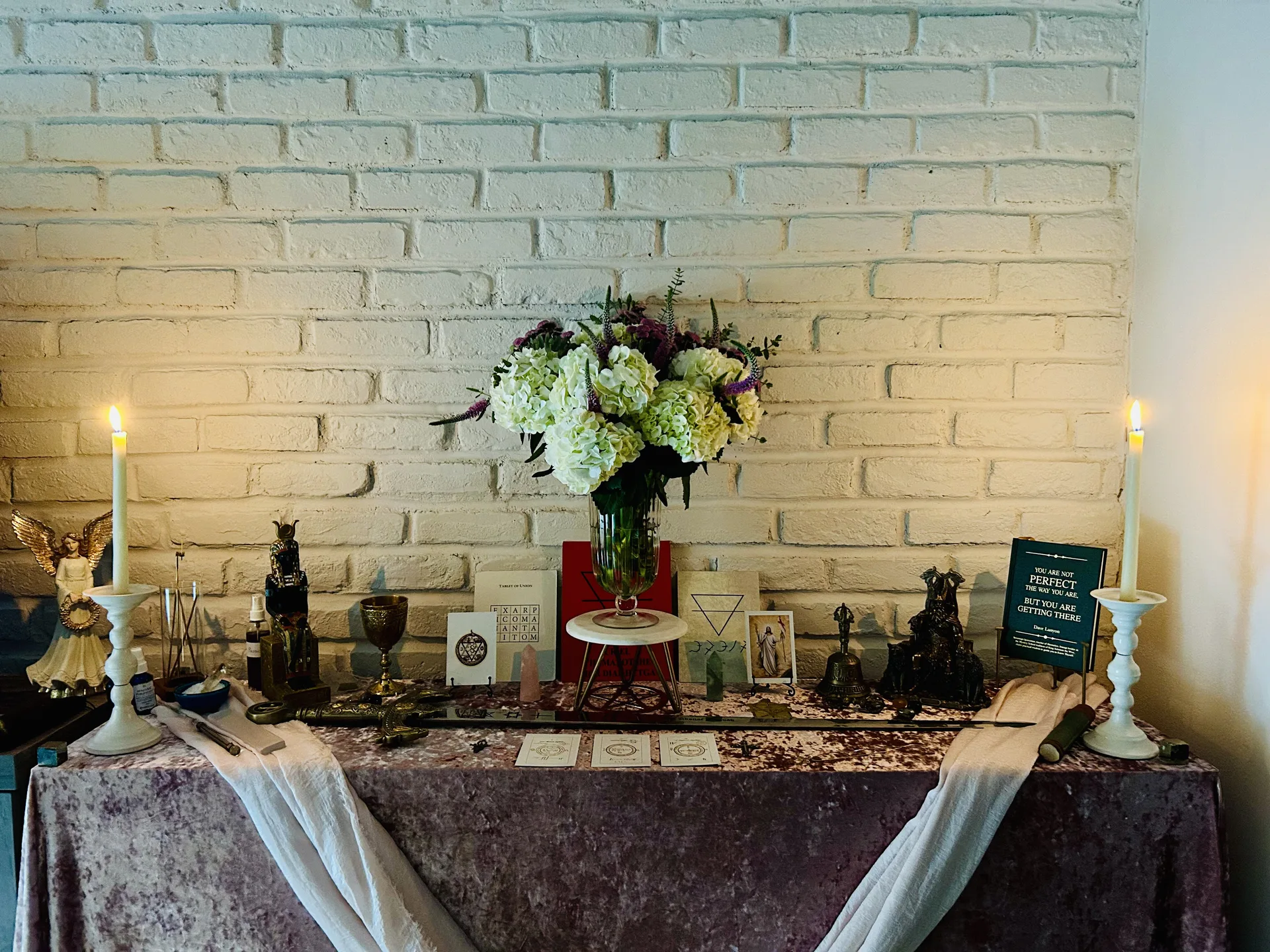 Sacred altar with flowers, candles, and ritual tools against a white brick wall